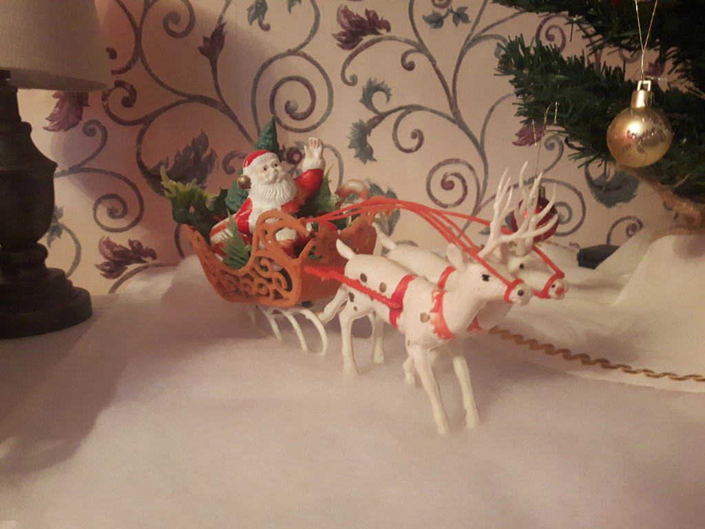 An old plastic ornament of Santa in his sleigh with 2 reindeer pulling it