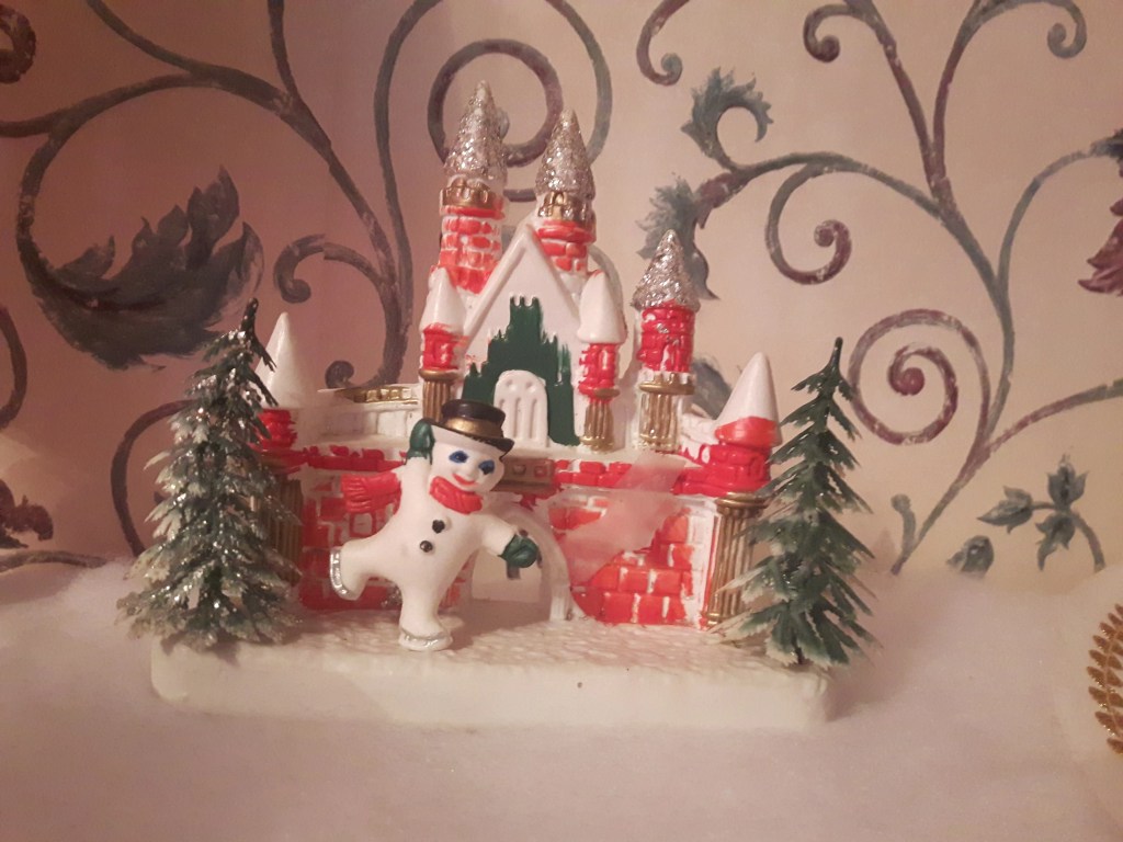 An old plastic decoration featuring Frosty the snowman skating in front of a Christmas castle with two trees.