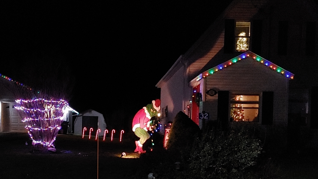 An image of outdoor Christmas decorations with the Grinch stealing the lights off the house.