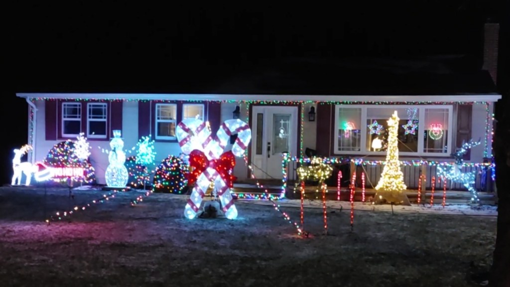An image of 2 giant candy canes glowing brightly in front of house decorated with Christmas lights